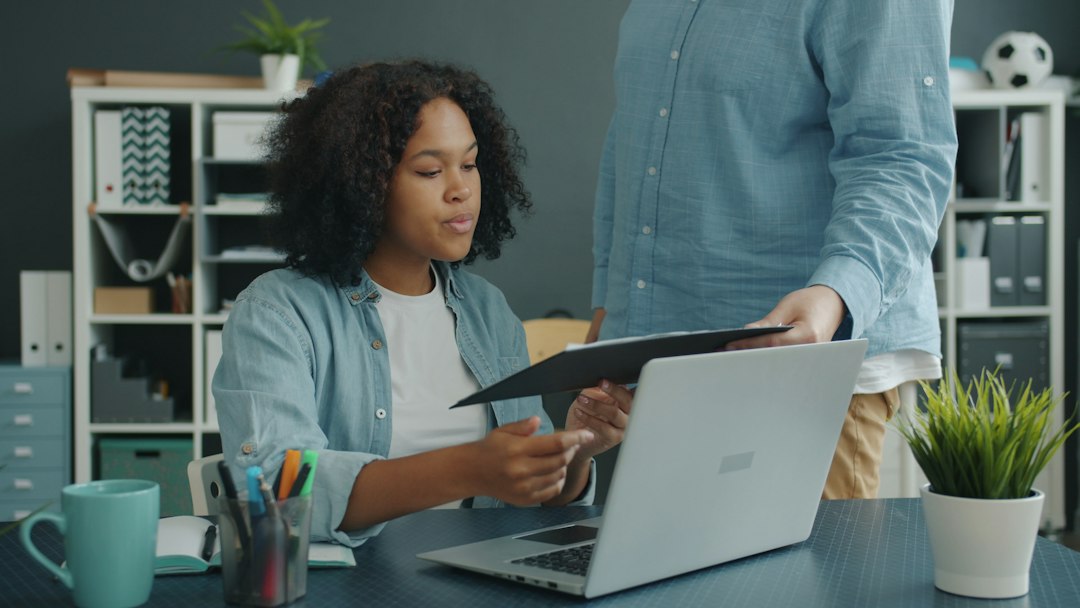 Due persone confrontano documenti cartacei accanto a un computer portatile